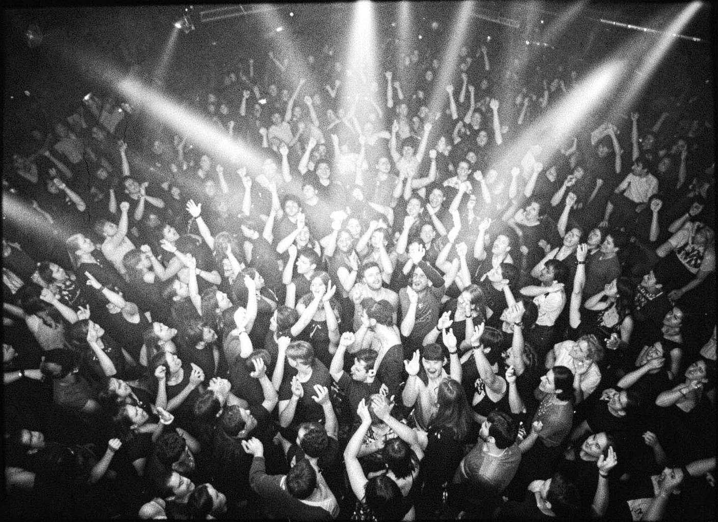 Black and white crowd dancing with hands in the air under stage lights